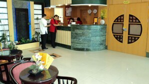 A reception area with a marble counter, wooden paneling, and a clock. There are chairs and a table with a vase of flowers. - Hotel Sogo Cabanatuan (Cabanatuan)