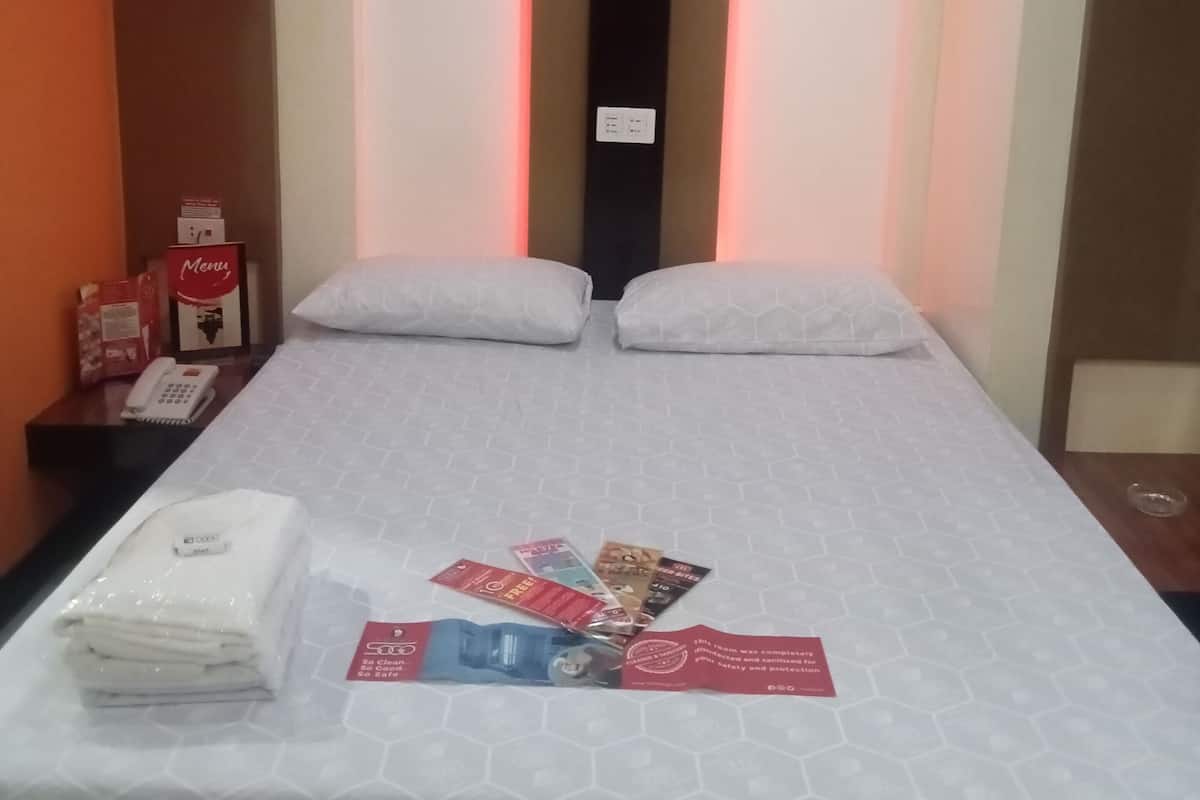 Habitación de hotel con cama, almohadas, mesita de noche con teléfono y carta, y unidad de aire acondicionado.