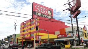 A hotel with a prominent red and yellow facade, a visible drive-in service sign, and a Jollibee restaurant adjacent to it. - Hotel Sogo Cabanatuan (Cabanatuan)