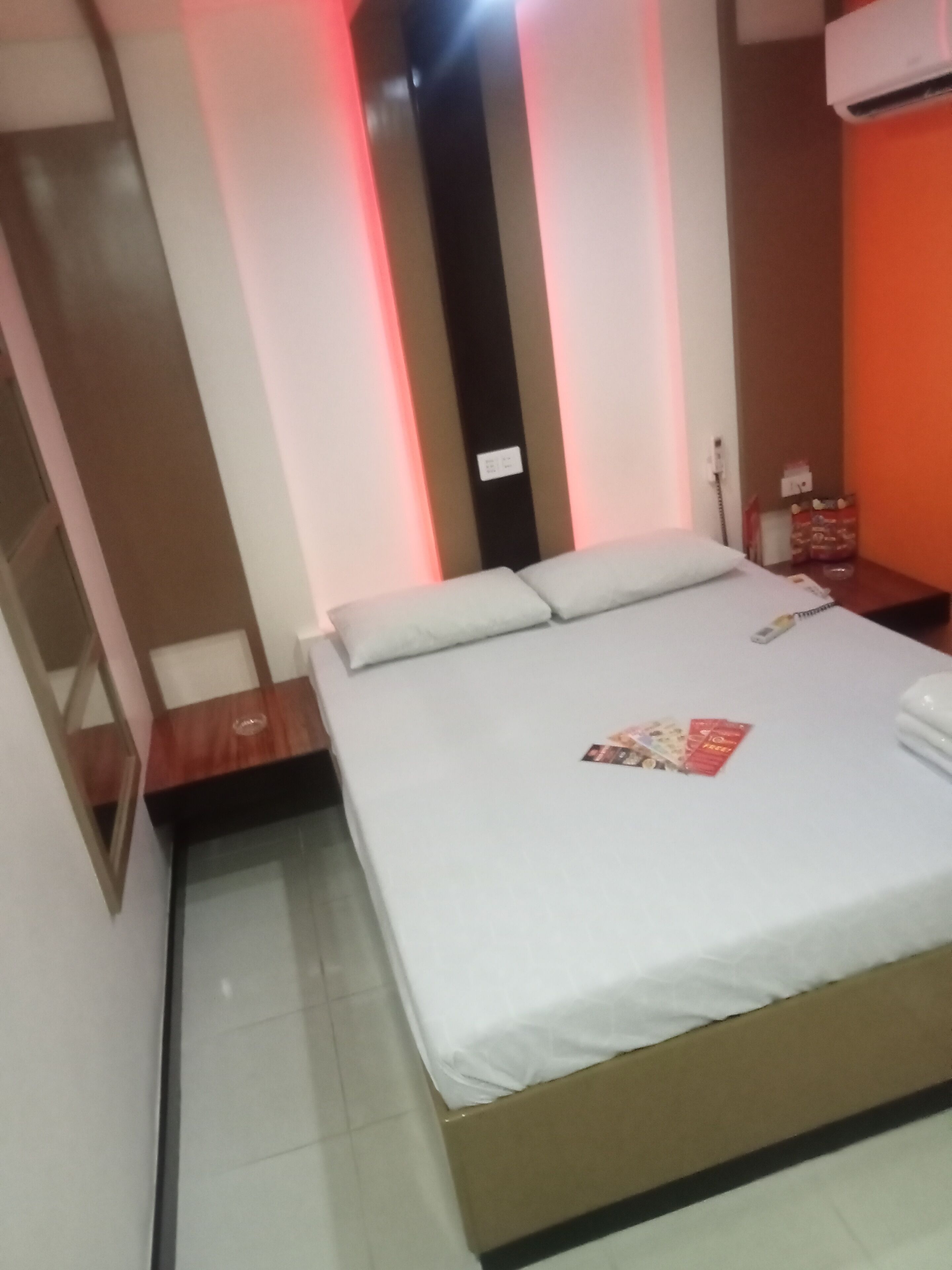A neatly made bed with a white mattress and pillows, a bedside table with a lamp, and a wall-mounted air conditioner.