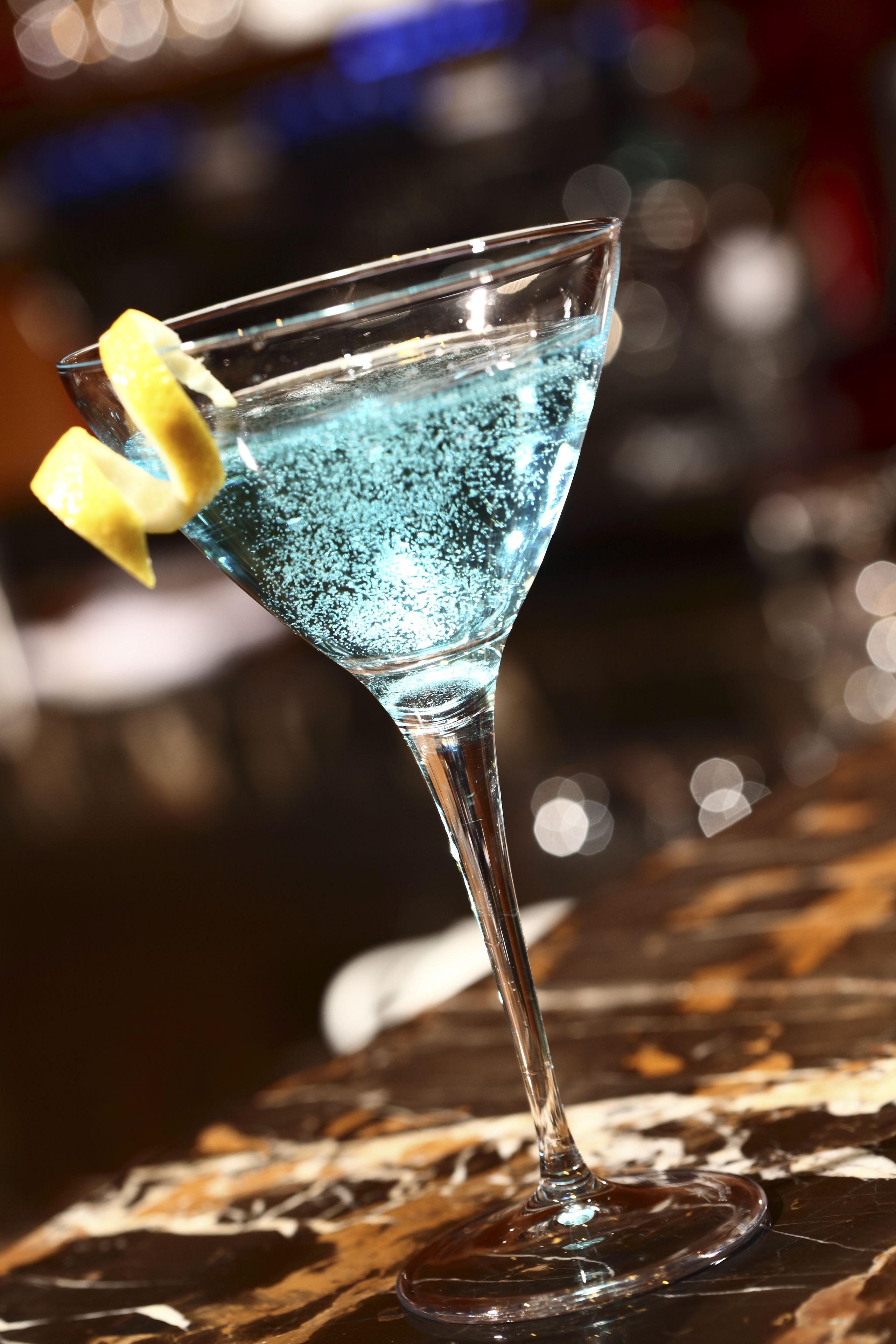 Una copa de martini con líquido azul y una rodaja de limón sobre una barra.