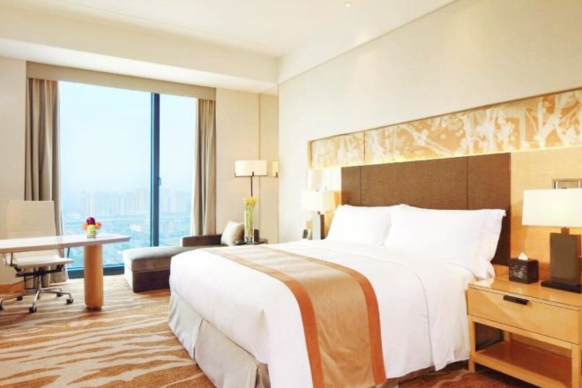 A hotel room with a large bed, a desk, and a view of the city.