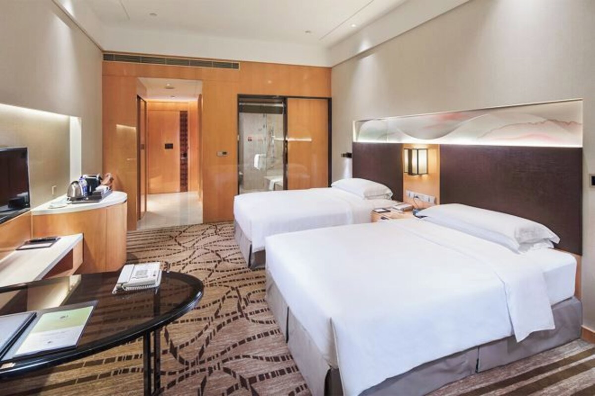 A hotel room with two beds, a desk with a chair, a television, and a reception area.