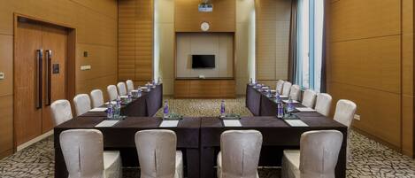 A conference room with a long table, chairs, a clock, and a television on the wall.