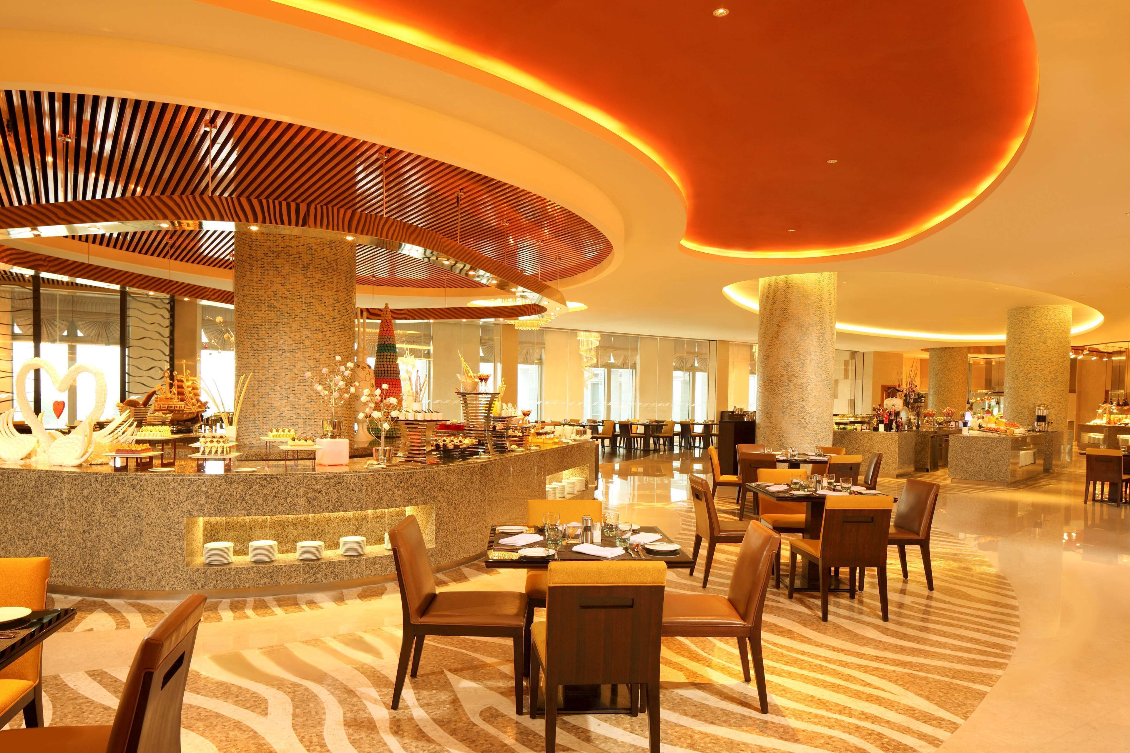 A spacious hotel lobby with a central bar area, multiple seating arrangements, and a modern design with a curved ceiling and illuminated columns.