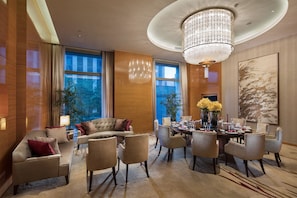 A modern hotel room with a dining area, large windows, and a chandelier.