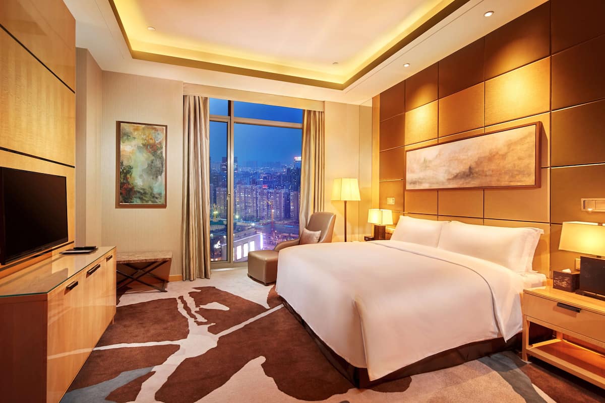 Une chambre d’hôtel avec un grand lit, une télévision, un bureau et une vue sur la ville la nuit.