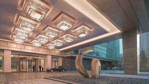 A modern building entrance with a revolving door, a large abstract sculpture, and a car parked outside. - Shangri-La Shenyang (Shenyang)