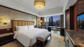 Quarto de hotel com cama grande, escrivaninha, cadeira, banqueta, televisão e vista para a cidade.