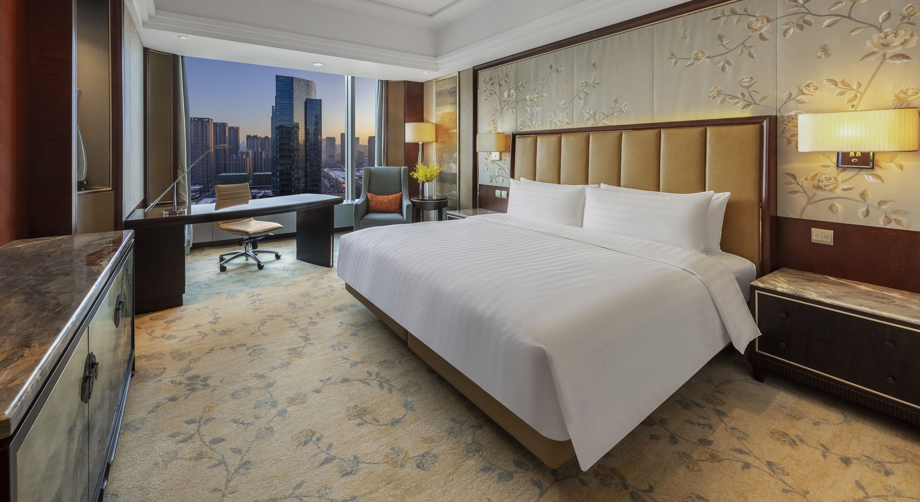 A hotel room with a large bed, a desk, and a view of a cityscape.
