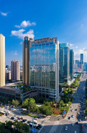 A modern high-rise building with a glass facade, surrounded by other tall buildings and a busy road with vehicles. - Shangri-La Shenyang (Shenyang)