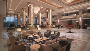 A spacious lobby with high ceilings, ornate columns, and a grand chandelier. There are seating areas with sofas and tables, and a piano in the background. - Shangri-La Shenyang (Shenyang)