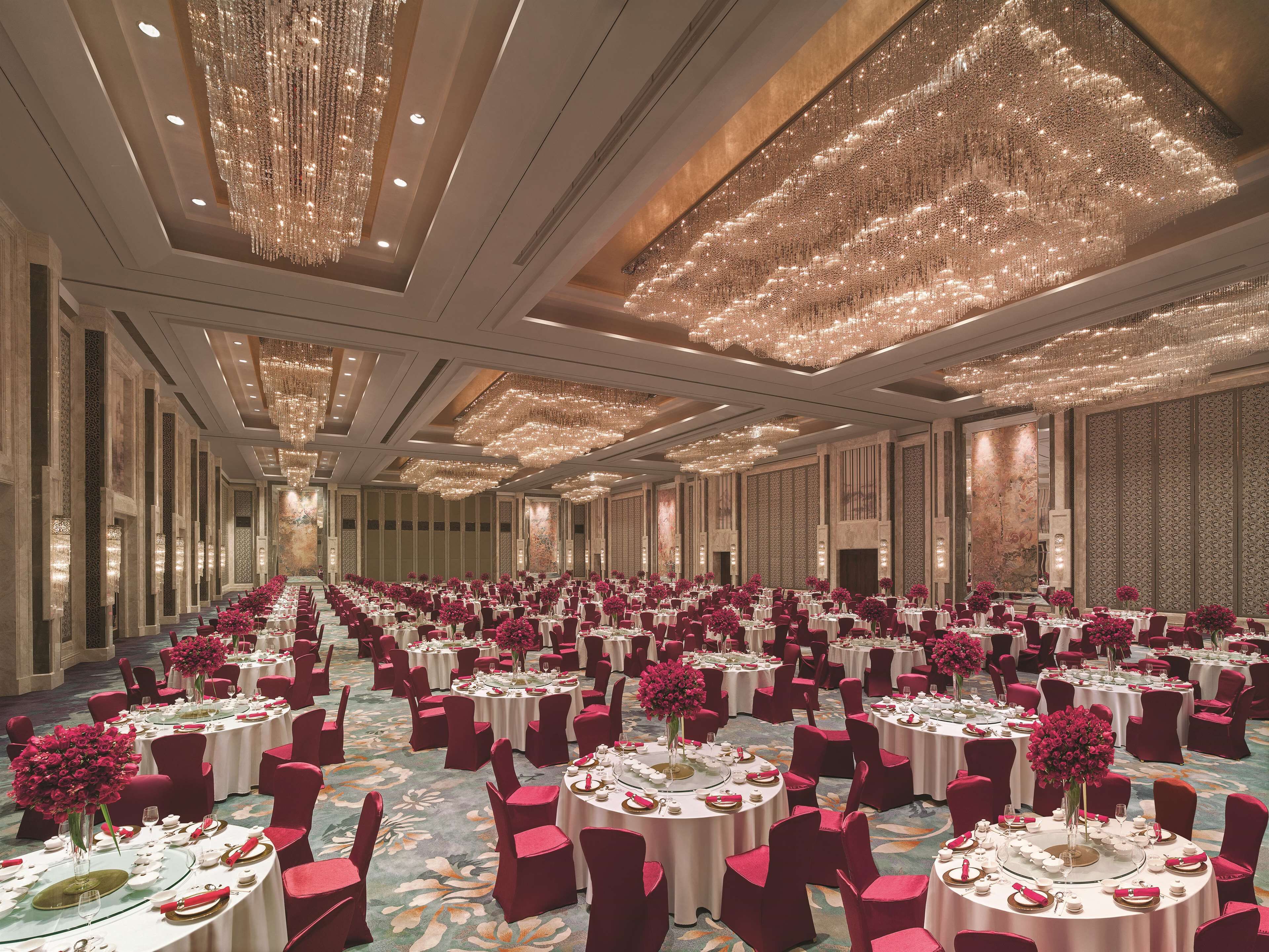 A large banquet hall with round tables, red chairs, and floral centerpieces.