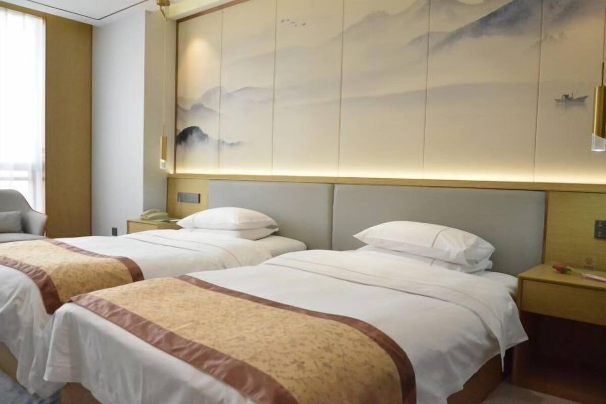 Quarto de hotel com duas camas, uma obra de arte na parede e uma mesa de cabeceira com abajur.