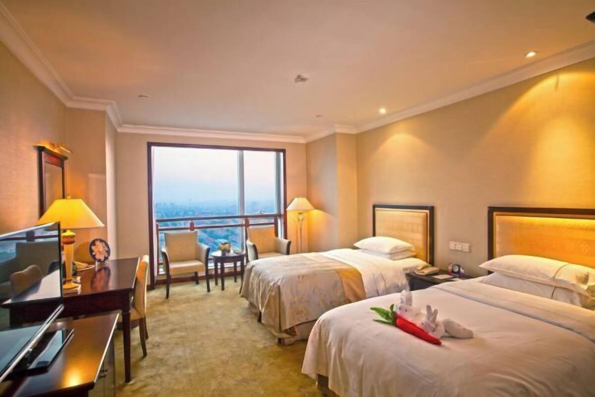 Quarto de hotel com duas camas, uma escrivaninha, uma cadeira, uma televisão e varanda com vista.