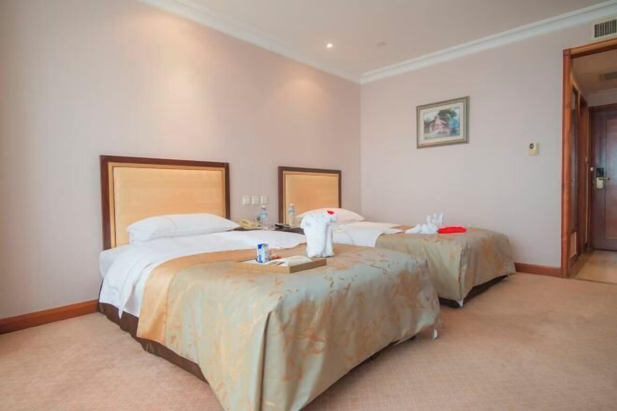 A hotel room with two beds, a painting on the wall, and a door to the right.