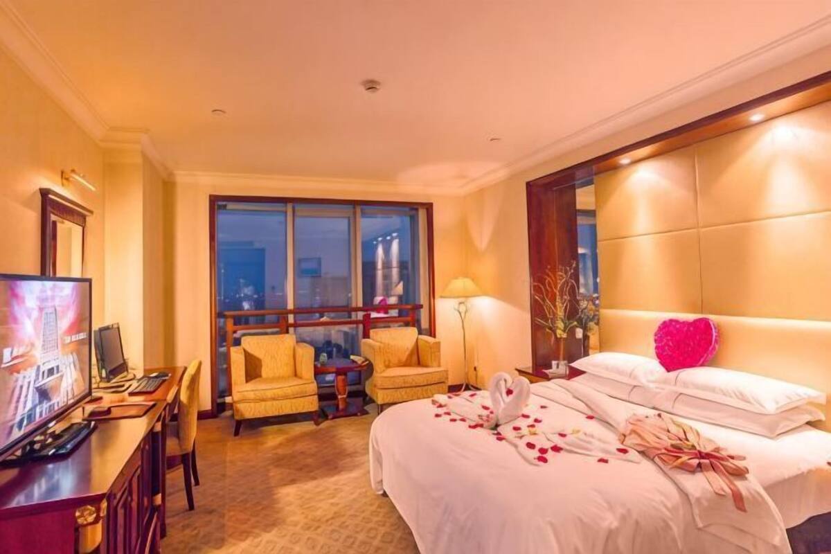 Quarto de hotel com cama, escrivaninha, televis ão e janela com vista para a cidade.