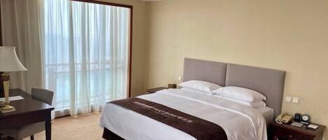 Habitación de hotel con una cama grande, un escritorio, una silla, una mesita de noche y una ventana con cortinas.