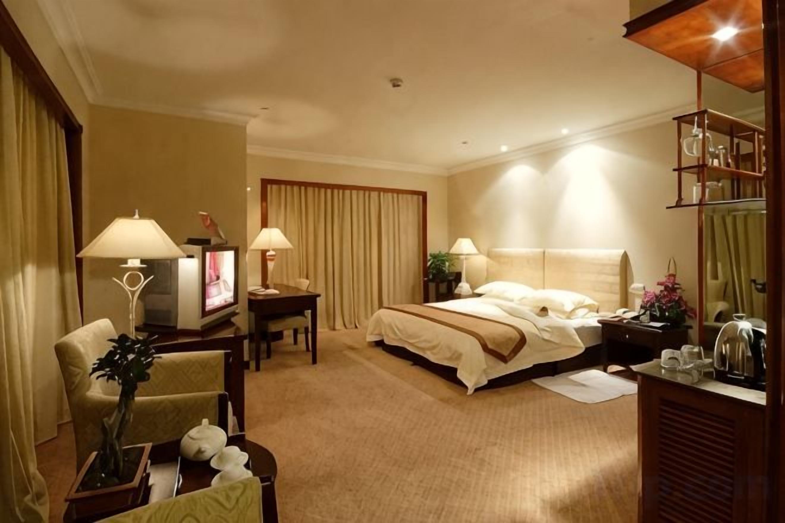 A hotel room with a bed, two bedside tables, a desk, a chair, and a television.