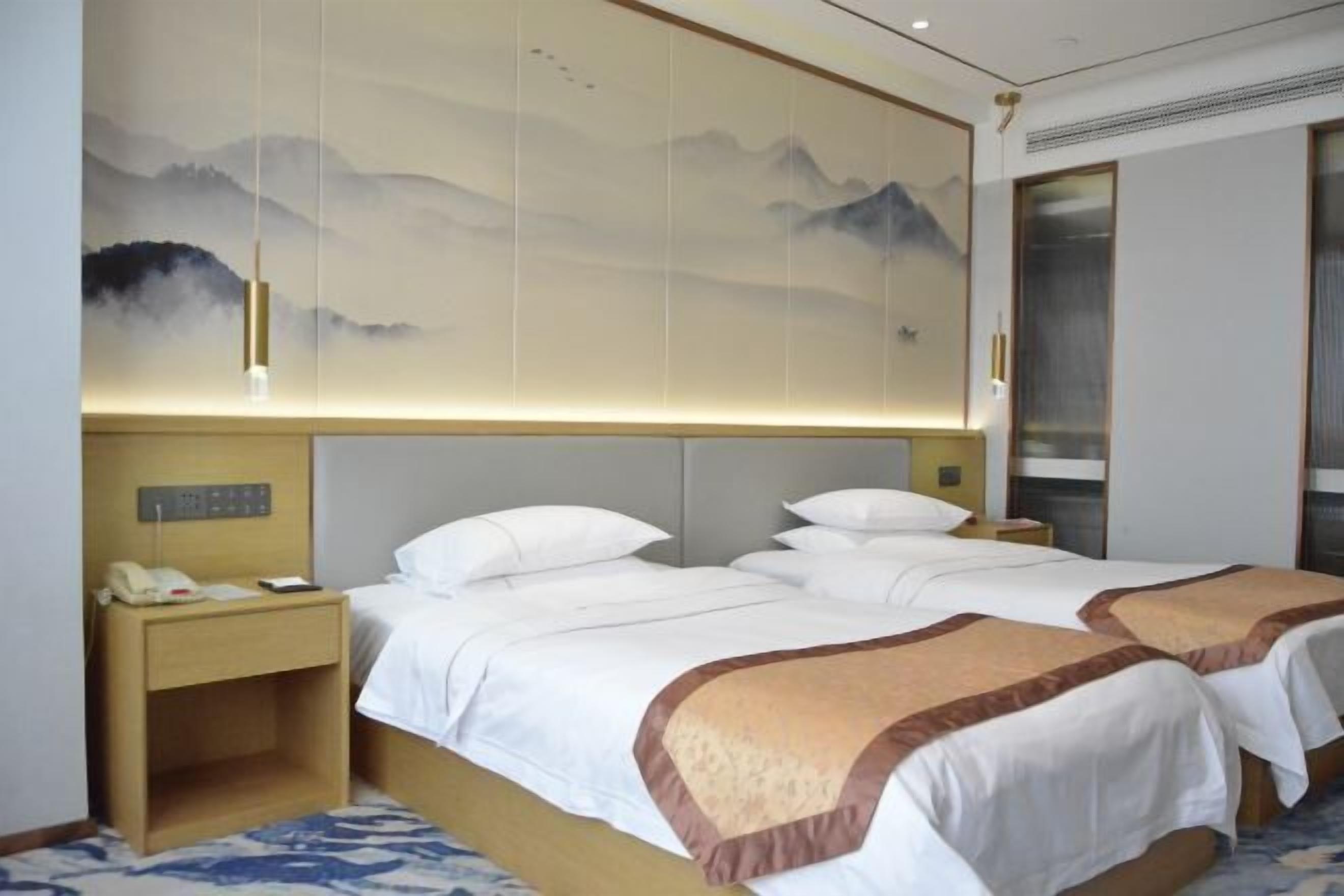 A hotel room with two beds, a nightstand, a wall-mounted phone, and a large painting of mountains.