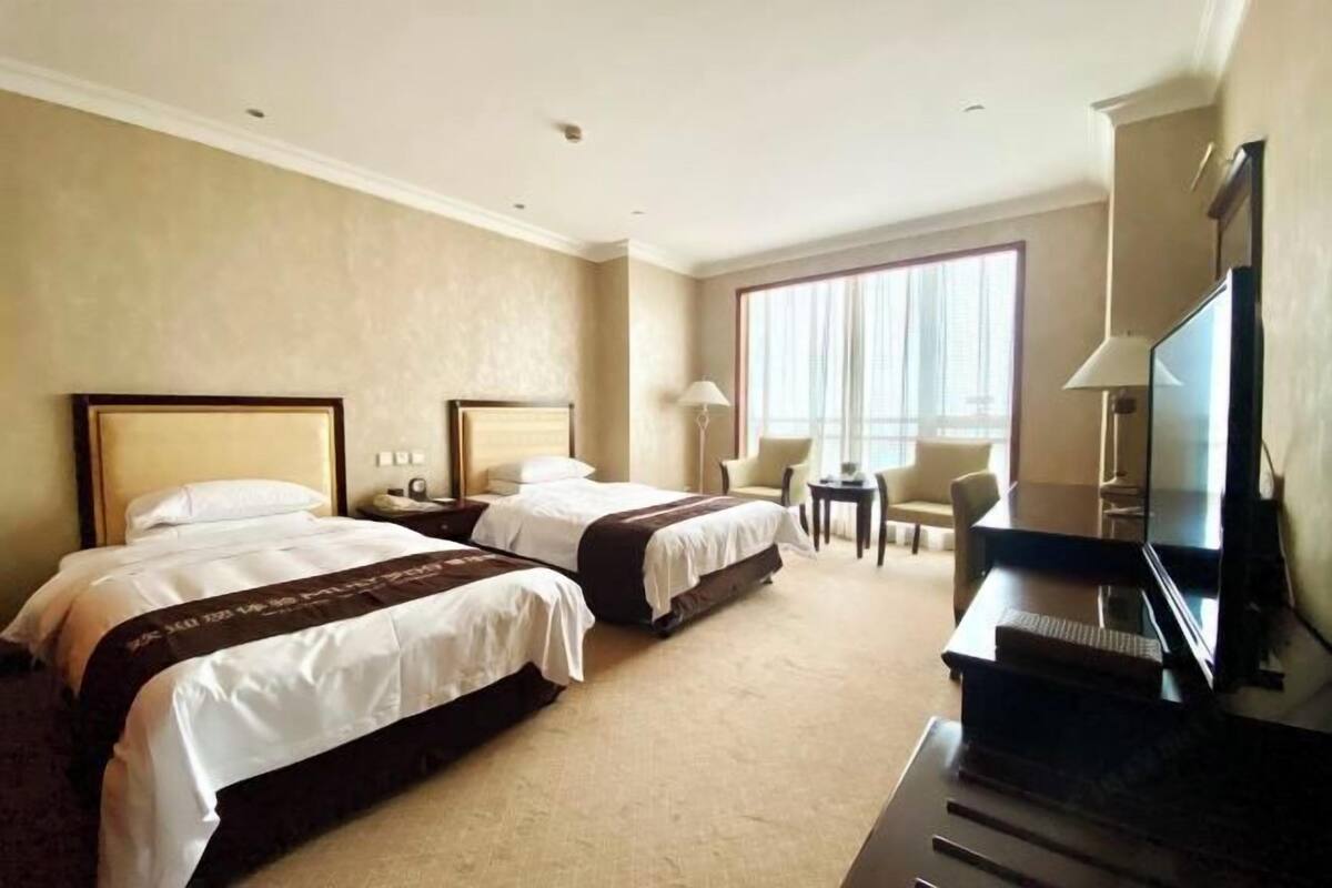 Quarto de hotel com duas camas, uma mesa, uma cadeira, televisão e janela com cortinas.