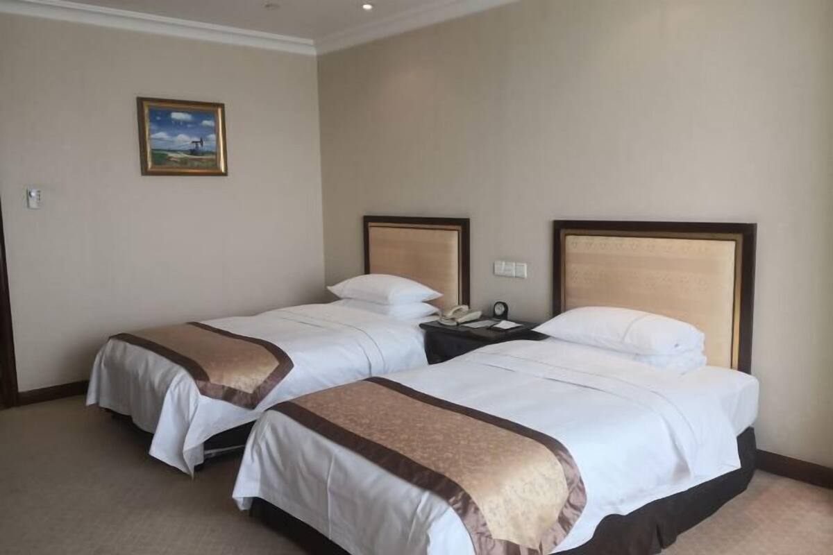 Quarto de hotel com duas camas, uma mesinha de cabeceira, um telefone e um quadro na parede.