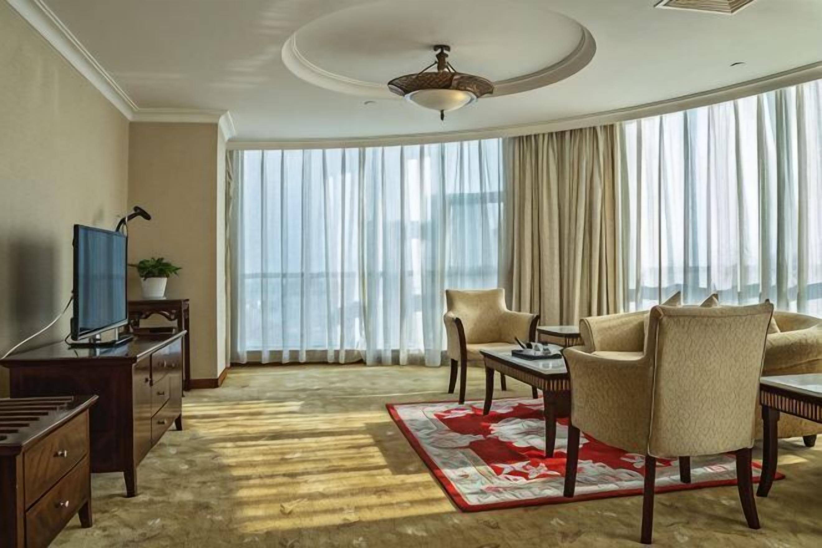 A living room with a television, a dining table, a sofa, and a large window with curtains.