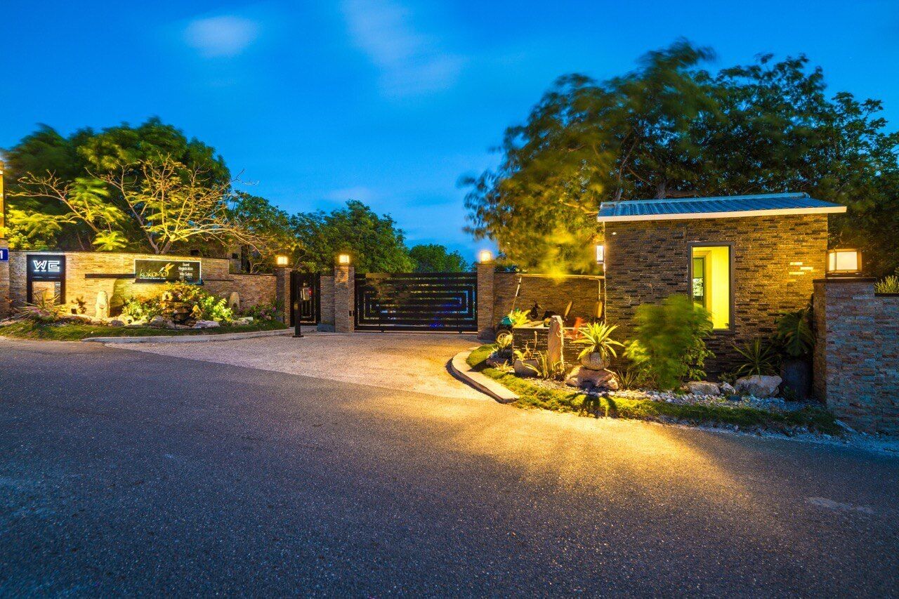 A gated entrance with a stone building, a signboard, and well-maintained landscaping.