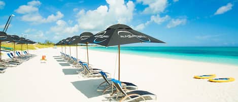 A beach with rows of sun loungers and umbrellas, a clear blue sky, and turquoise water.
