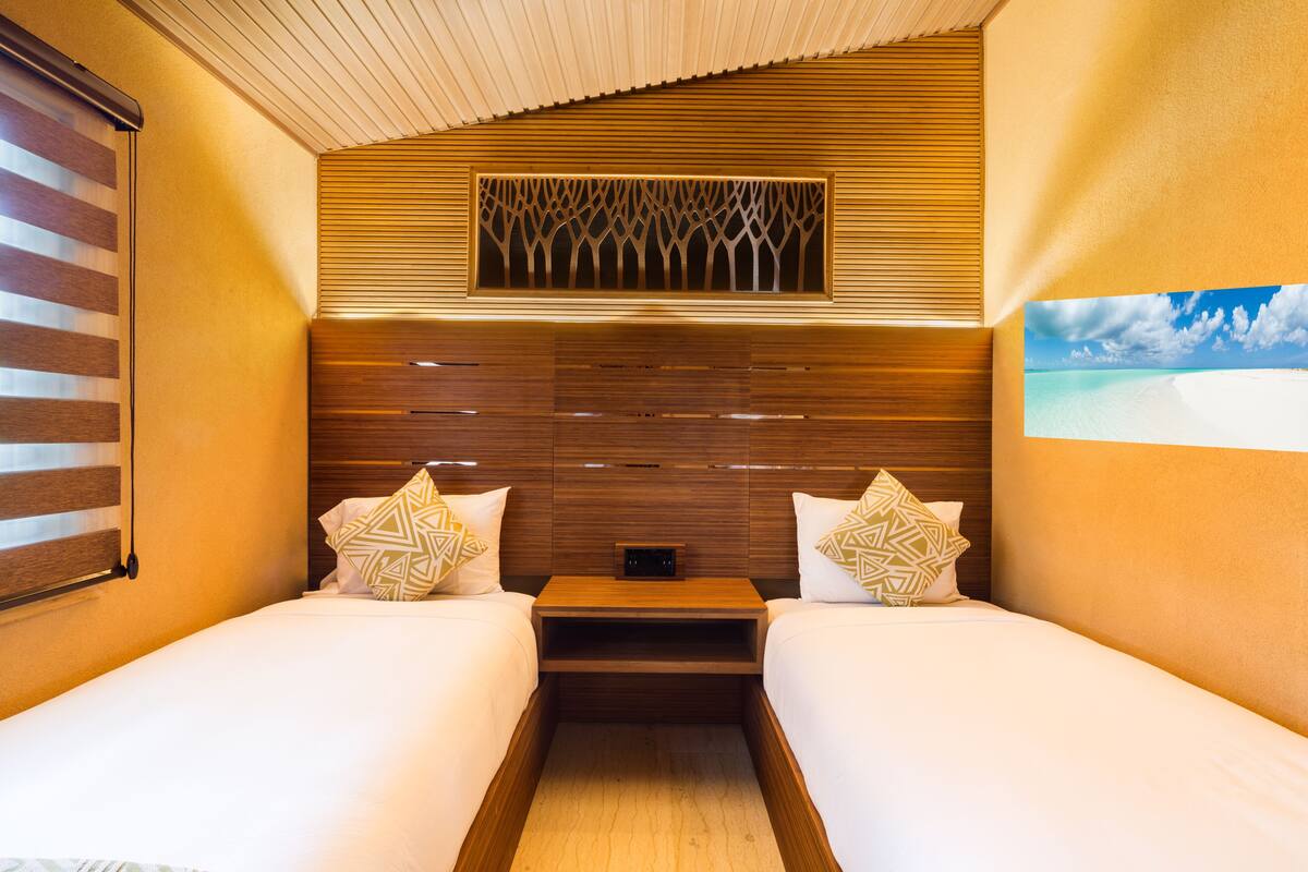 Ein Hotelzimmer mit zwei Betten, Holz-Kopfteilen, einer eingebauten Ablage und einem Fenster mit Blick auf einen Strand.