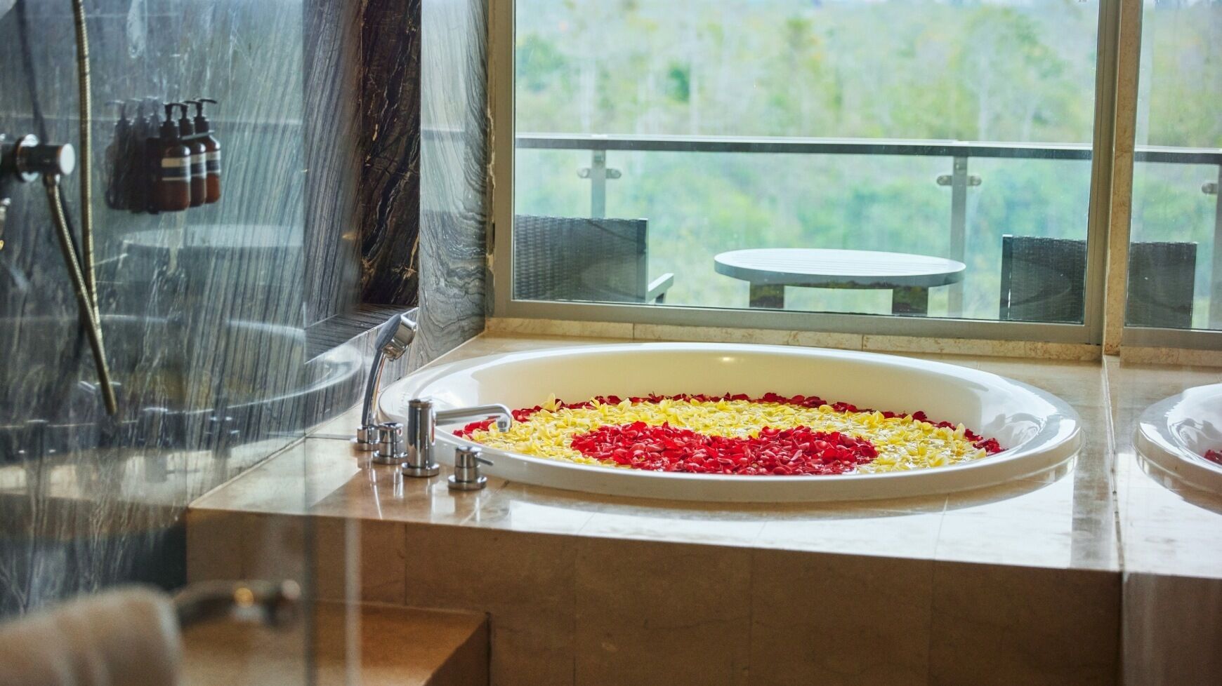 Un baño con una bañera grande llena de pétalos de rosa, ducha y vistas al exterior.