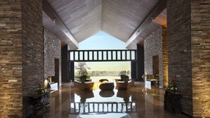 A spacious lobby with a high ceiling, stone walls, and a large seating area with a view of the outdoors. - RIMBA by AYANA Bali (Jimbaran)