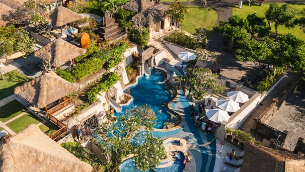 An aerial view of a resort with multiple swimming pools, a central water feature, and surrounding lush greenery. - RIMBA by AYANA Bali (Jimbaran)