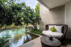 A modern outdoor seating area with a pool, surrounded by lush greenery.