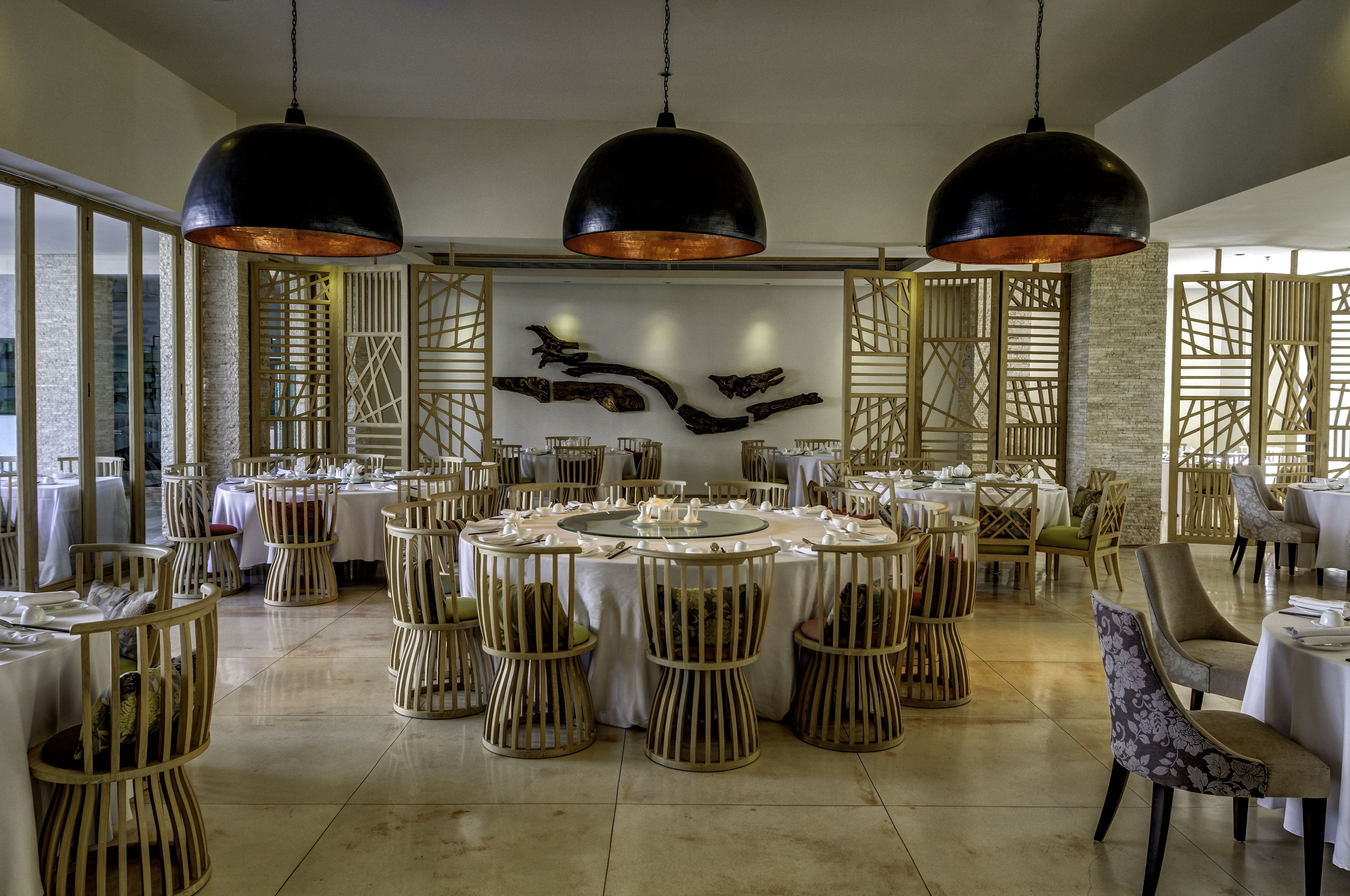 A spacious dining area with round tables, wooden chairs, and black pendant lighting.