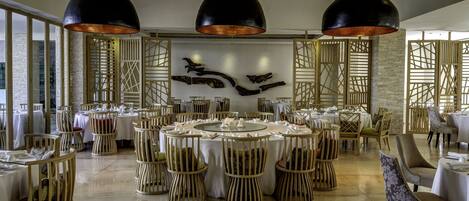 A spacious dining area with round tables, wooden chairs, and black pendant lighting.
