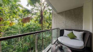 A balcony with a wicker chair and a small round table, overlooking a lush garden with various plants and trees.