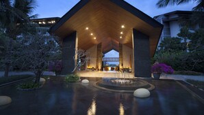 A modern building with a wooden roof and stone pillars, surrounded by a water feature and tropical plants. - RIMBA by AYANA Bali (Jimbaran)