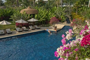 A swimming pool with lounge chairs and umbrellas, surrounded by lush greenery and flowers. - RIMBA by AYANA Bali (Jimbaran)