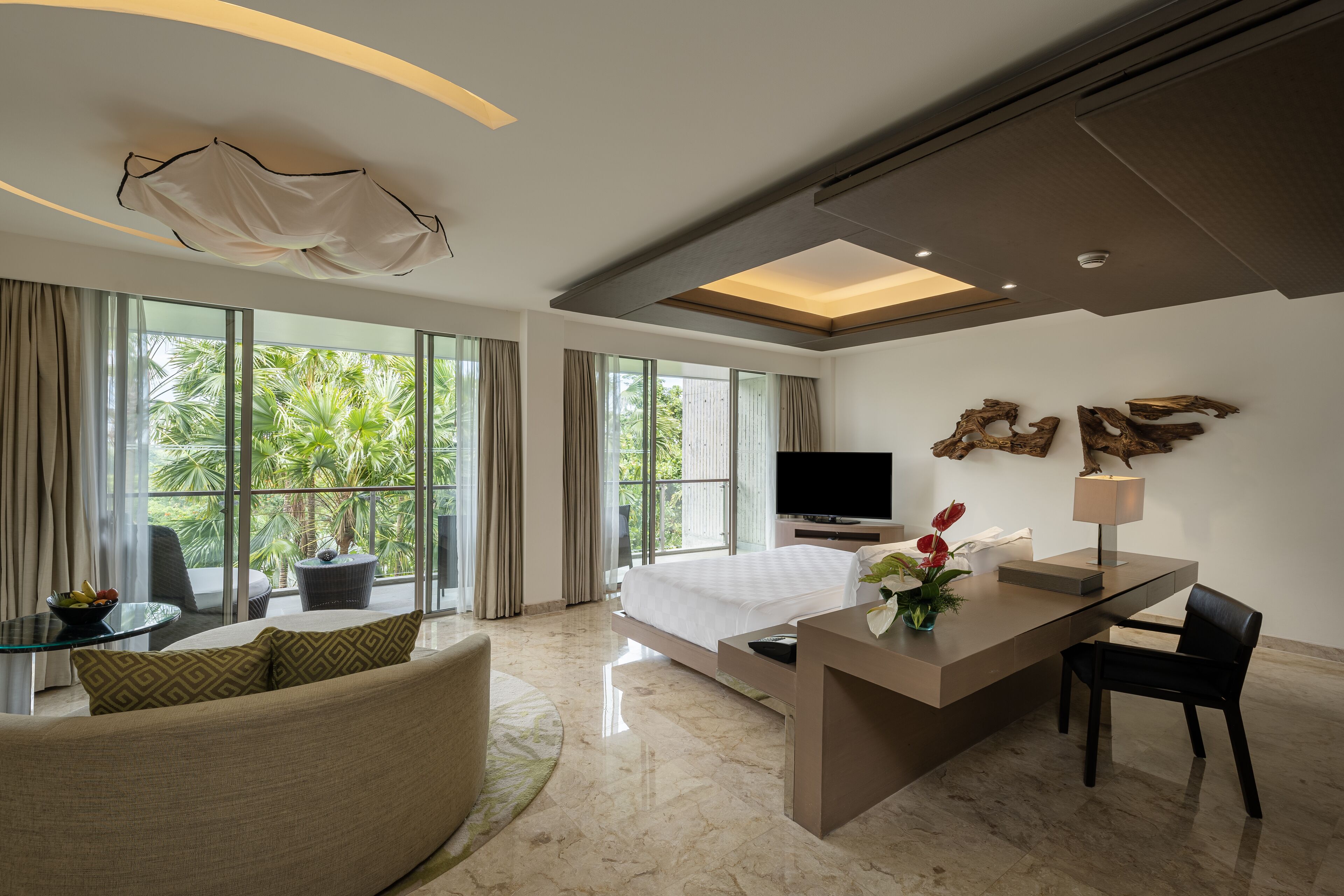Quarto de hotel moderno com uma cama grande, televisão, secretária com abajur e um sofá.