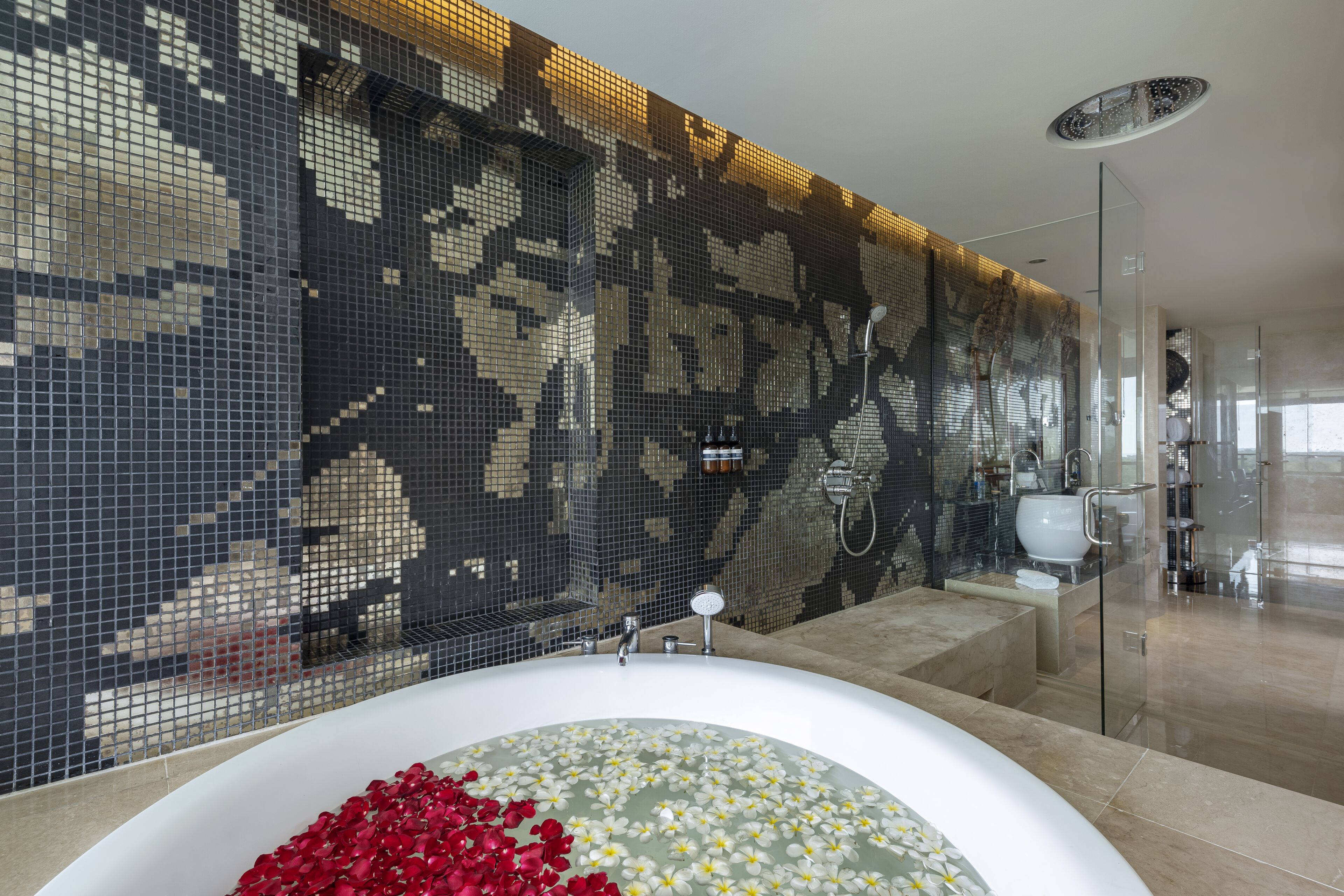 A modern bathroom with a large bathtub, mosaic wall tiles, and a glass shower enclosure.