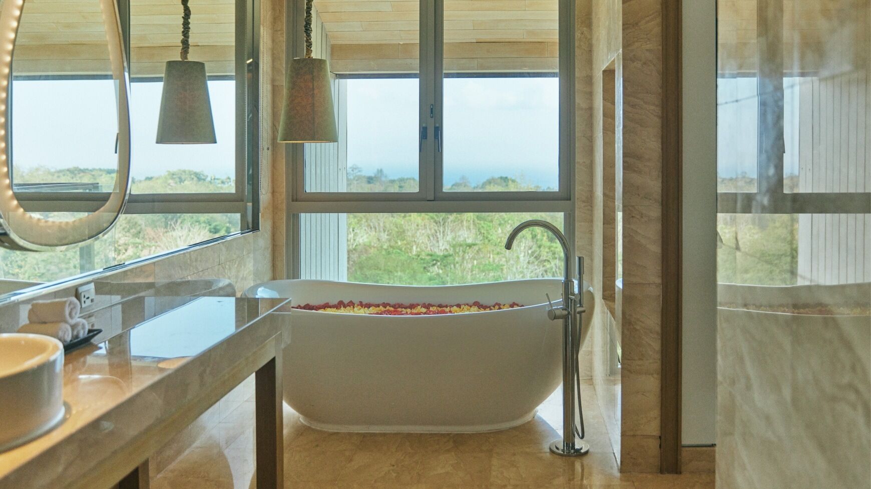 Un baño moderno con una bañera independiente, un espejo grande y vistas a zonas verdes al exterior.