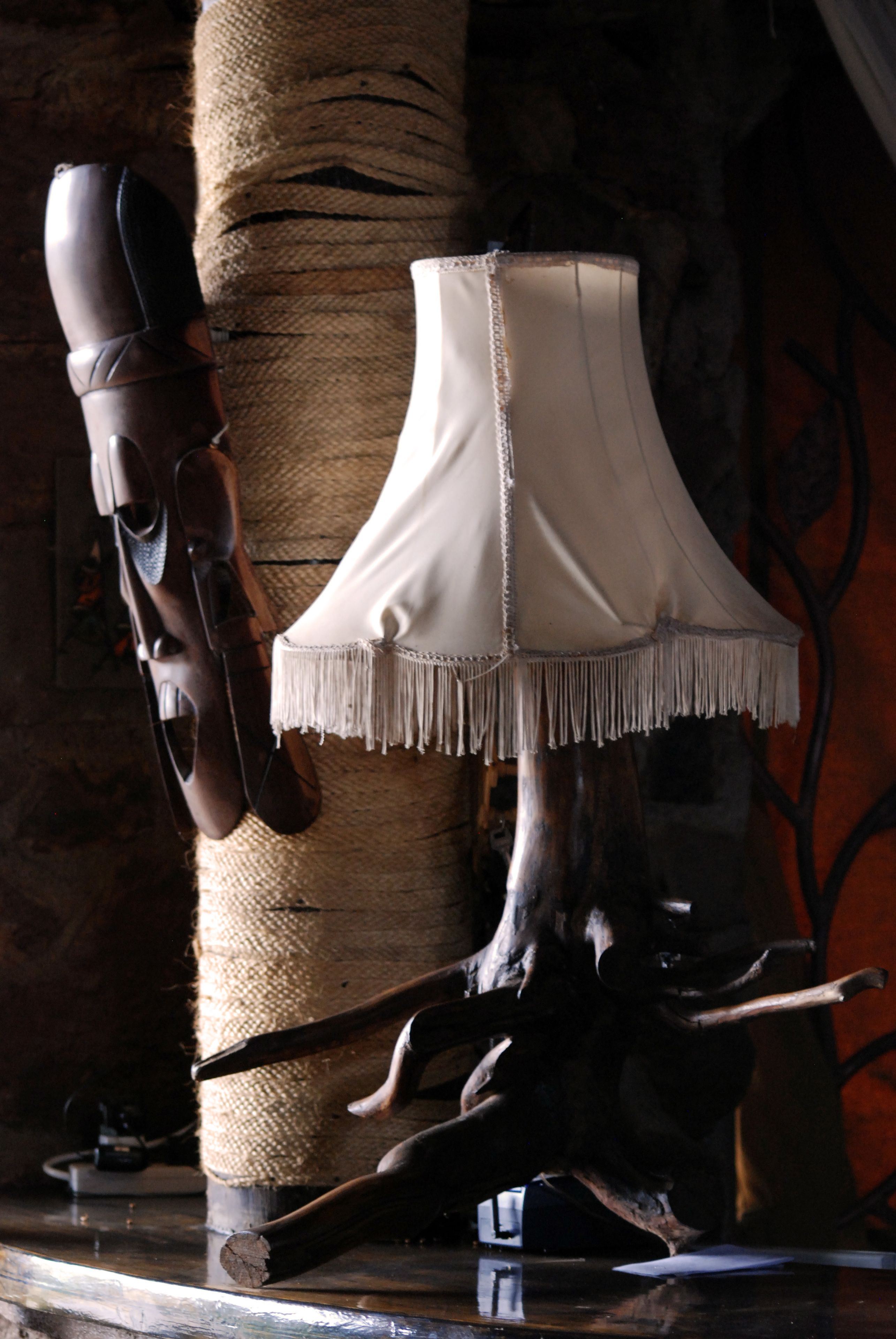 A rustic interior with a wooden sculpture, a pair of boots, and a lamp with a fringed shade.