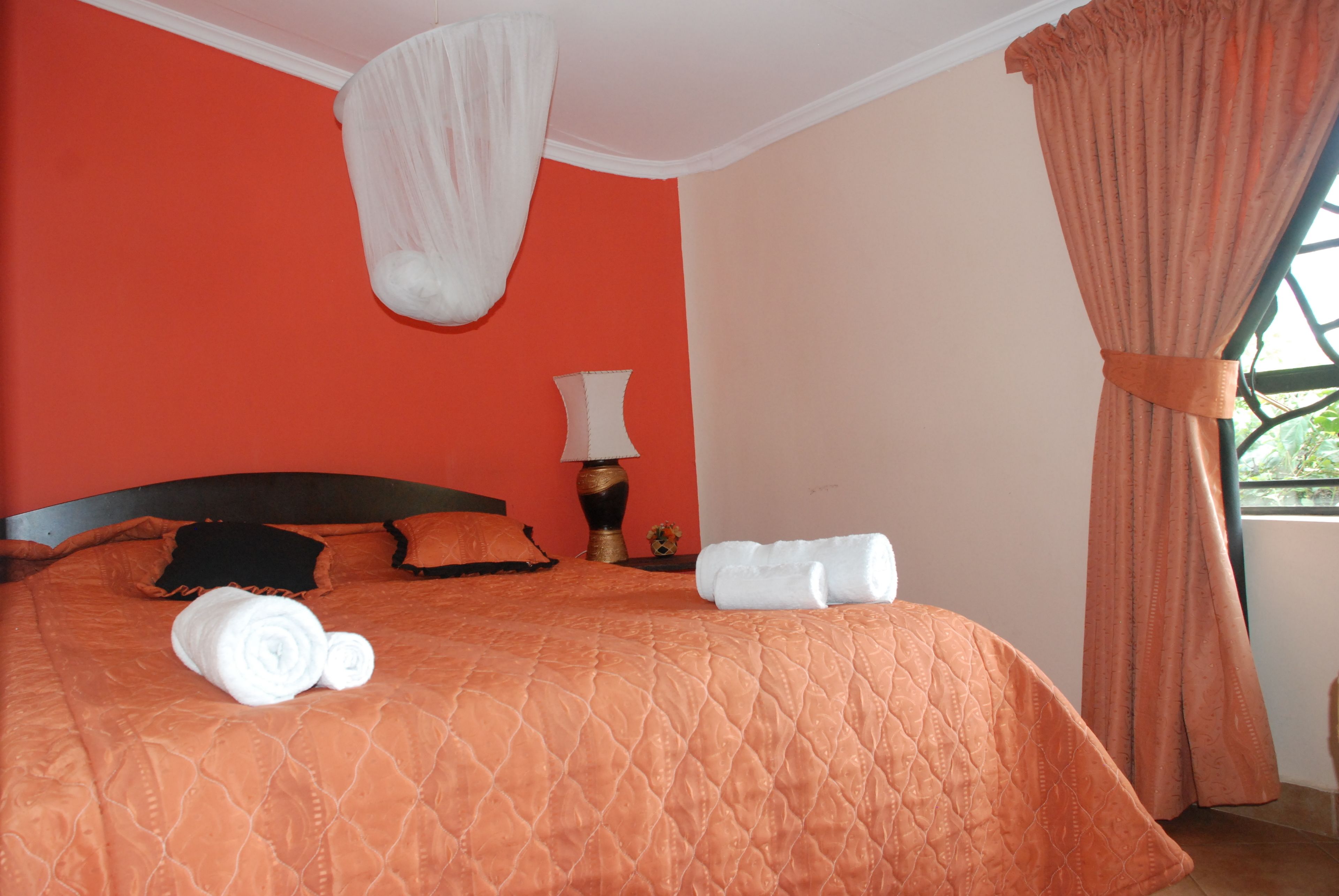 A hotel room with a large bed, orange bedding, a canopy, and a window with curtains.