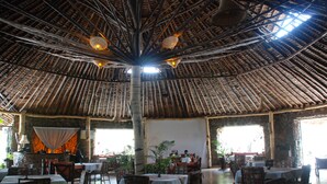 A restaurant with a thatched roof, tables set for dining, and large windows allowing natural light. - Osoita Lodge (Ongata Rongai)