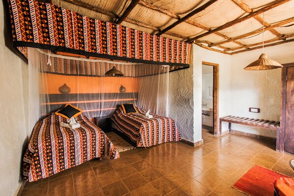A room with two beds, a bench, and a hanging light fixture.