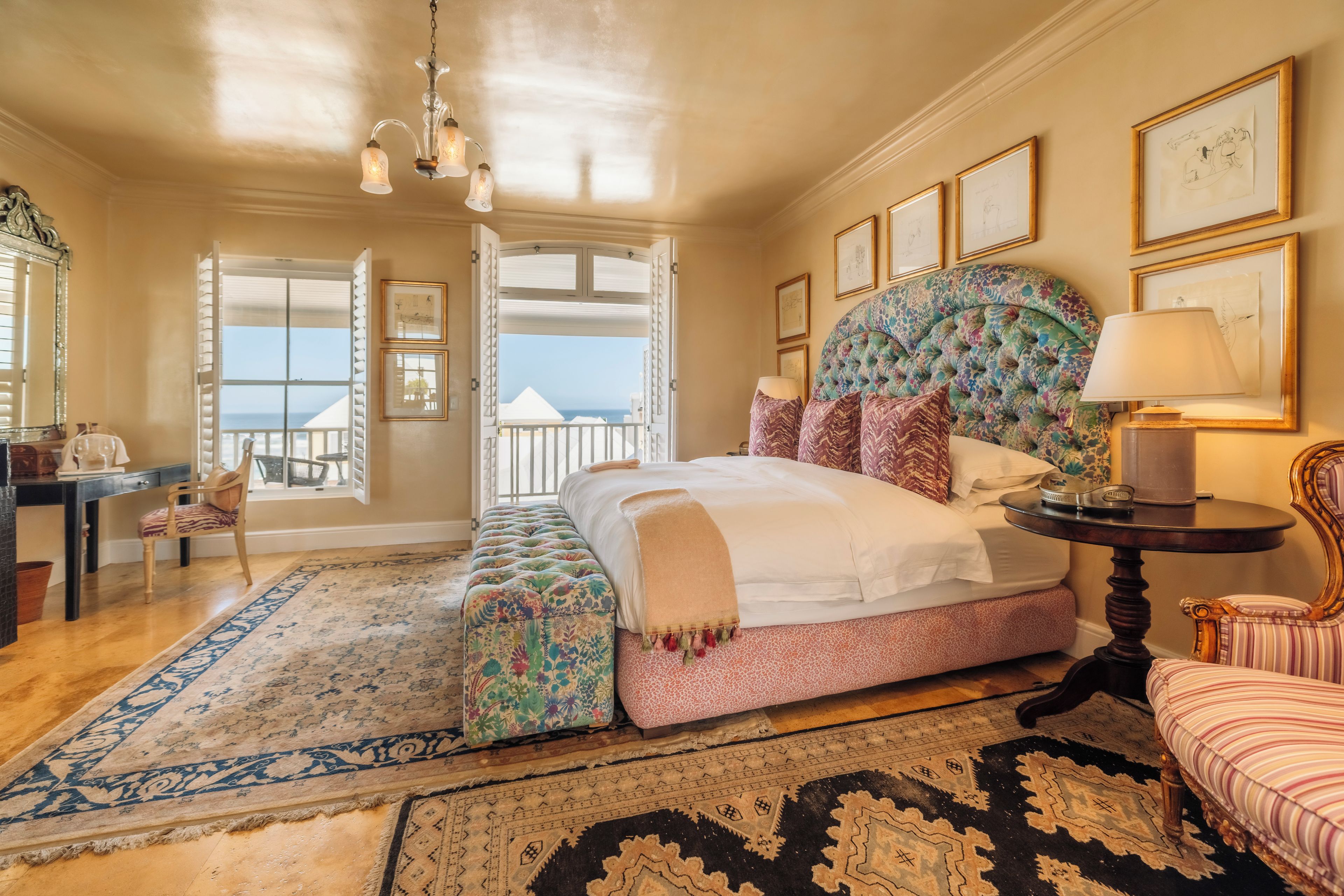 A spacious bedroom with a large bed, a bench, a desk, and a view of the sea.