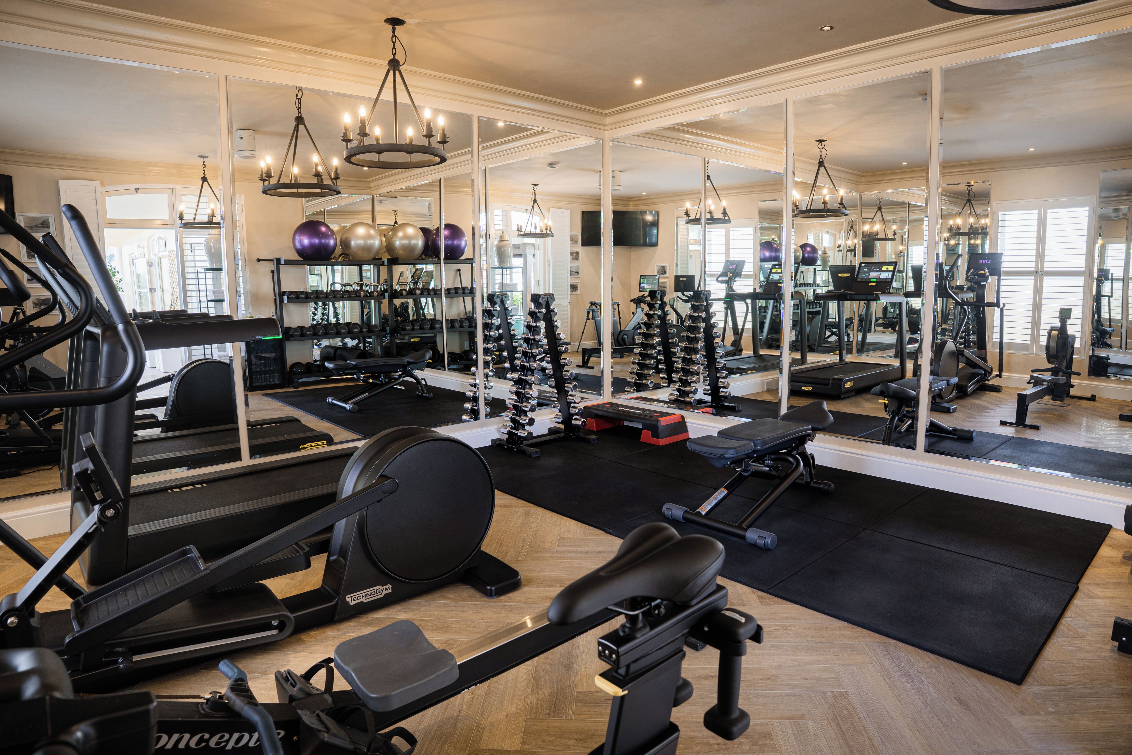 Un gimnasio con equipamiento de ejercicio, espejos y suelo de madera.