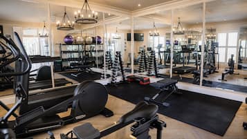 Un gimnasio con equipamiento de ejercicio, espejos y suelo de madera.