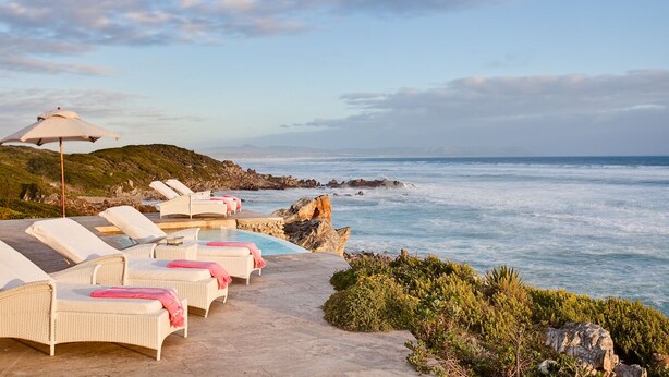 A beachside lounge area with white wicker chairs and pink towels, overlooking the ocean. - Birkenhead House (Hermanus)